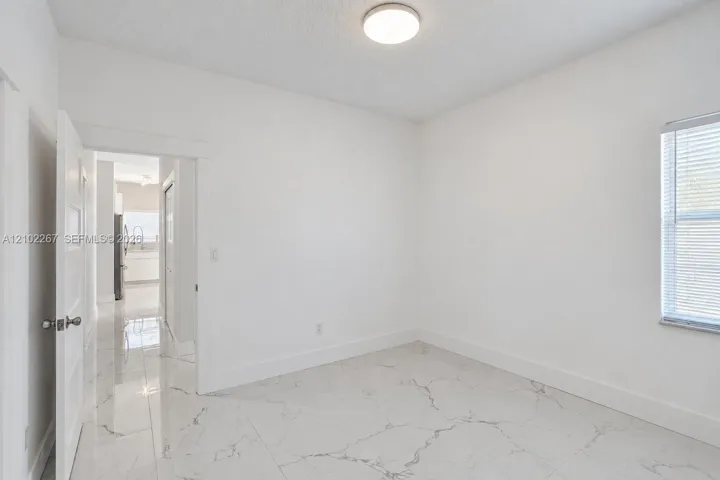 Interior room featuring polished large-format tile flooring with veining, flush-mount ceiling lighting, and a window with horizontal blinds
