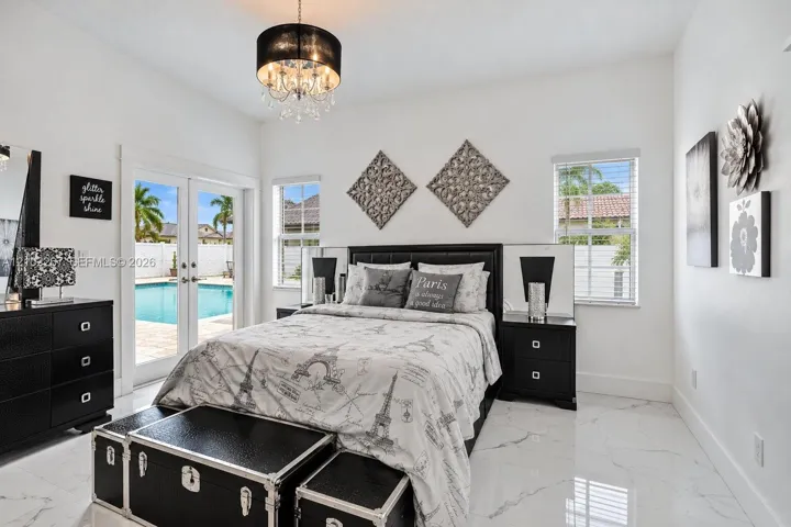 Neutral-toned large format tile flooring, drum-style crystal chandelier, and glass-paneled double doors featuring a view of the pool