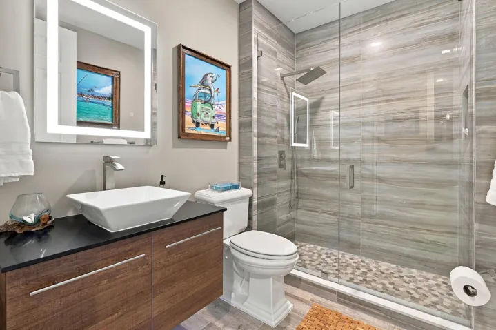 Guest bath features a floating vanity with under lighting and vessel sink, frameless, walk-in glass shower with Rain Showerhead, pebble-like flooring and built-in shower niche, and an LED, de-fog mirror.