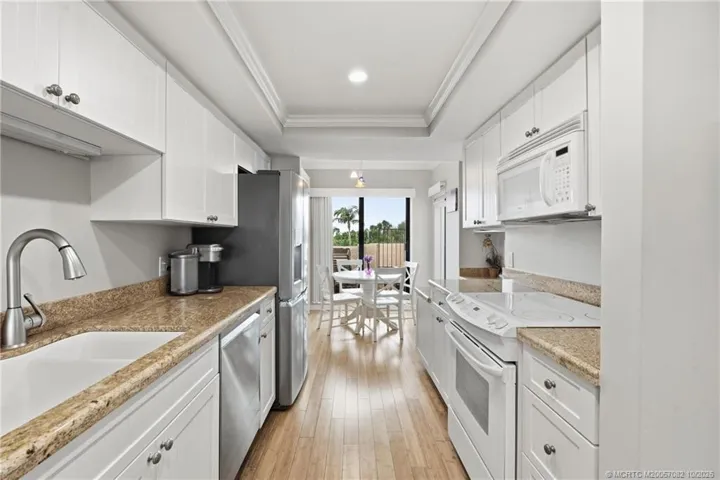 Bright galley-style kitchen with white cabinetry, granite countertops and stainless-steel appliances.
