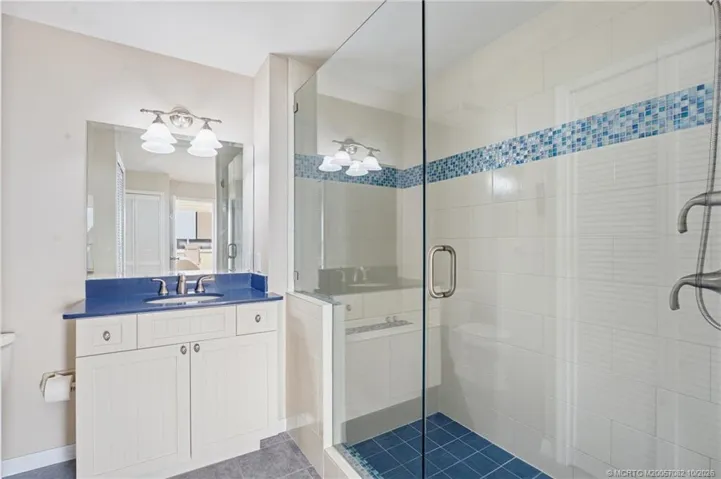 Walk-in shower with frameless glass enclosure, tiled walls, blue mosaic accents, and handheld showerhead.