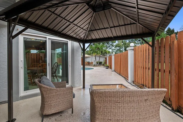 Covered patio area with a dark-finished metal gazebo, concrete flooring, and a wood privacy fence