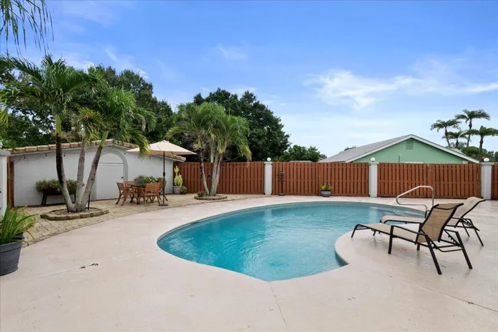 Freeform swimming pool with a surrounding concrete deck, wood-tone fencing, and mature palm trees