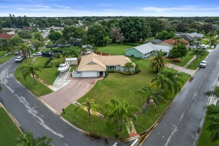 Expansive corner lot featuring a brick paver driveway, an attached garage, and mature palm trees