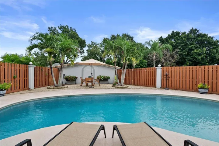 Curved swimming pool with a concrete surround, wood privacy fencing, and tropical landscaping