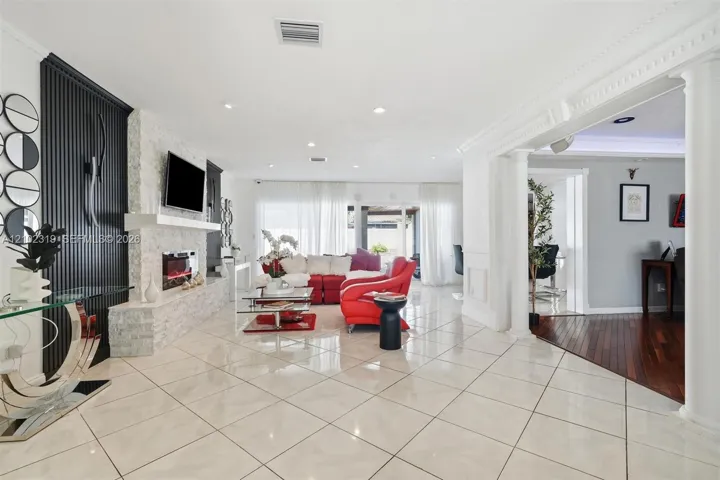 Living area featuring large-format tile flooring, a floor-to-ceiling textured accent wall, a stacked-stone fireplace, and decorative columns