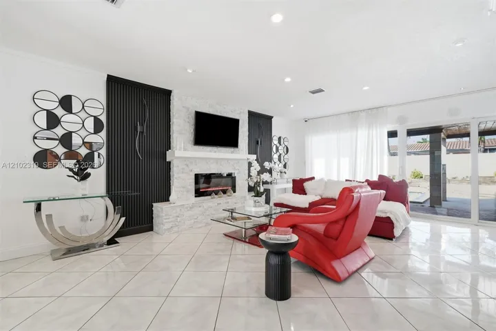 Living area featuring large-format tile flooring, a floor-to-ceiling stone-textured fireplace surround with a custom mantel, recessed lighting, and sliding glass doors