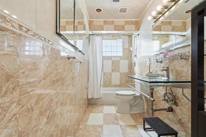 Bathroom featuring floor-to-ceiling stone-finish tilework, a glass-topped vanity with an undermount sink, a wall-spanning mirror, recessed lighting, and a glass-block window