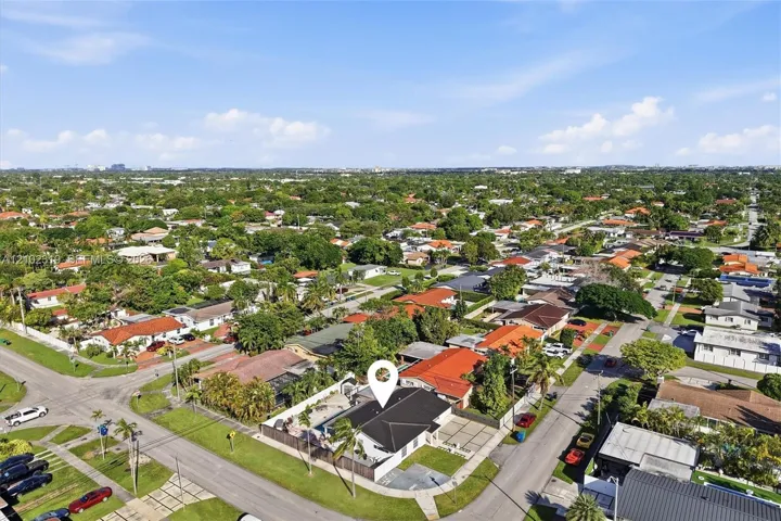 Aerial view of a residential corner lot featuring a multi-hipped roof, an inground swimming pool, a concrete driveway, and established perimeter landscaping