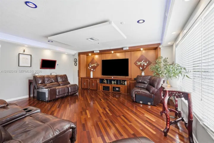 Living area featuring wood-finish flooring, custom built-in cabinetry with integrated lighting, recessed ceiling lighting, and crown molding