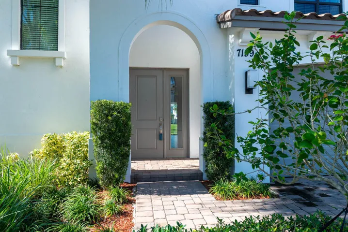 Arched entryway featuring double doors with glass lites, a paved walkway, and manicured landscaping