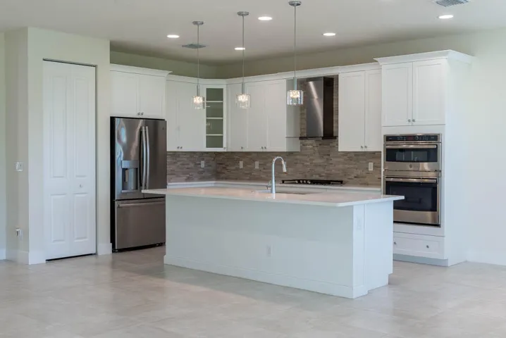 Kitchen featuring white cabinetry, stainless steel appliances, a center island with sink, and tile flooring