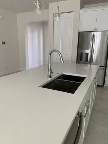 Kitchen island with a light-toned solid surface countertop, undermount double-basin sink, and chrome gooseneck faucet
