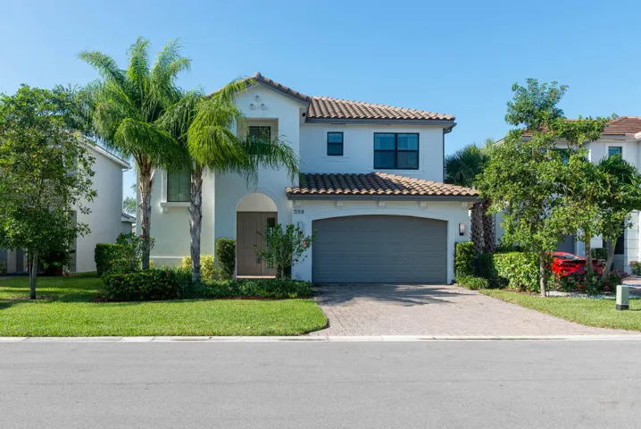 Stucco exterior with a tile roof, arched entry, paver driveway, and an attached two-car garage