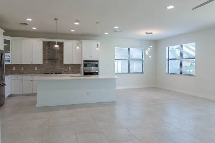 Kitchen island with pendant lighting, integrated stainless steel appliances, white cabinetry, and a textured backsplash