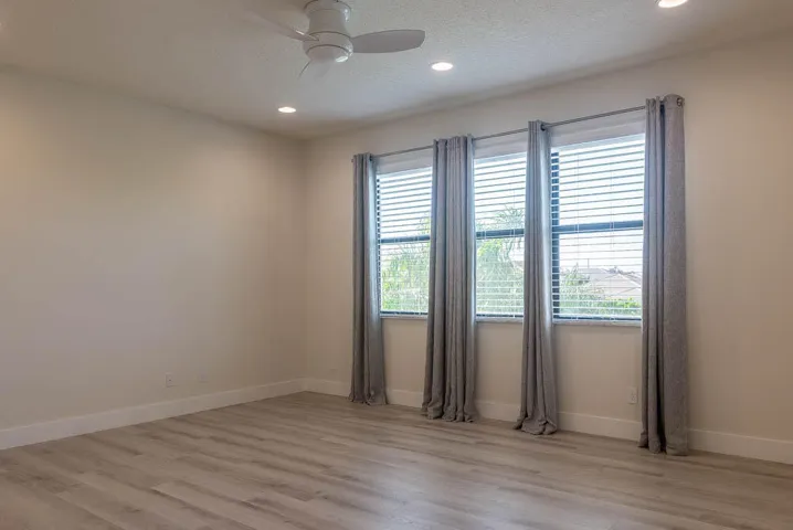 Recessed ceiling lighting, wood-finish flooring, ceiling fan with integrated lighting, three windows with blinds, and neutral wall tones