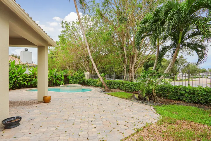 Paved patio featuring a round pool with an integrated spa, mature palm trees, and lush landscaping