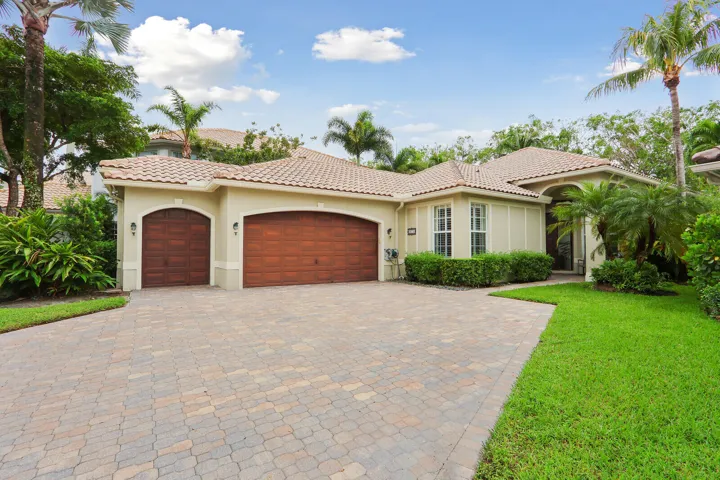 Stucco exterior with a tiled roof, paver driveway, arched garage doors, and established landscaping