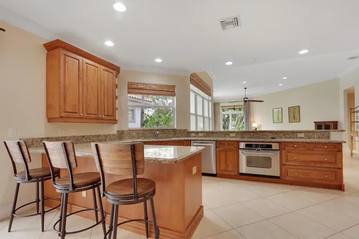 Kitchen featuring wood cabinetry, light-toned tile flooring, granite countertops, stainless steel built-in oven, and recessed lighting