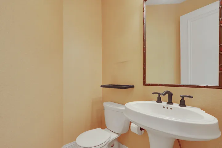 Pedestal sink with bronze-finish faucet, framed mirror, and toilet