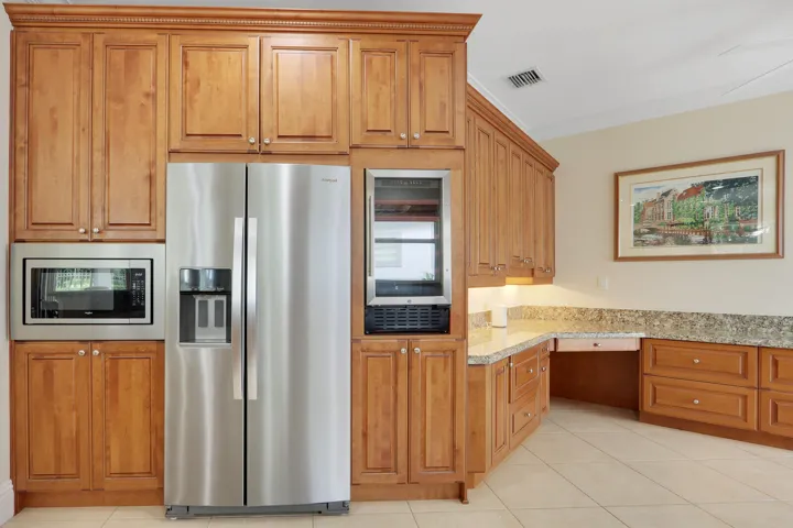 Maple cabinetry with crown molding, stainless steel side-by-side refrigerator, built-in microwave, stone countertops, and tile flooring
