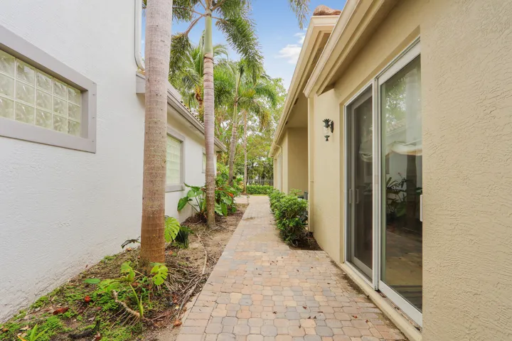 Paver walkway, mature palm trees, glass block window, sliding glass door, exterior wall sconce