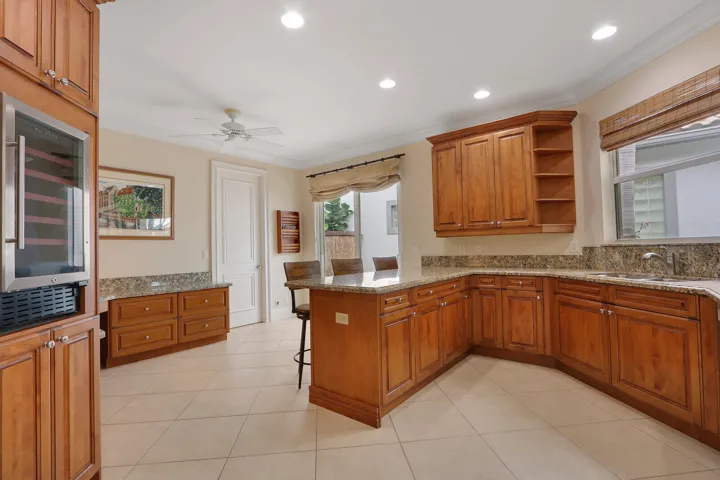 Expansive kitchen featuring wood cabinetry, stone countertops, a central island, integrated beverage cooler, and tiled flooring