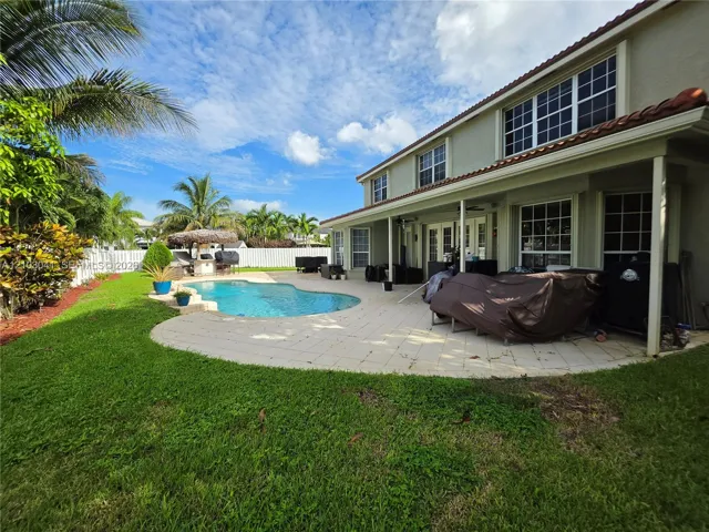 Expansive backyard featuring a free-form swimming pool, spacious paved patio, and a covered tiki bar