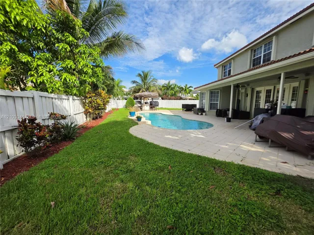 Expansive backyard featuring a manicured lawn, a white privacy fence, and mature trees