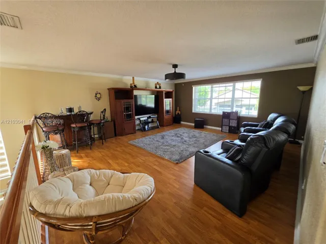 Wood-finish flooring throughout, ceiling fan with integrated lighting, multiple windows providing natural light, and a built-in wet bar with seating