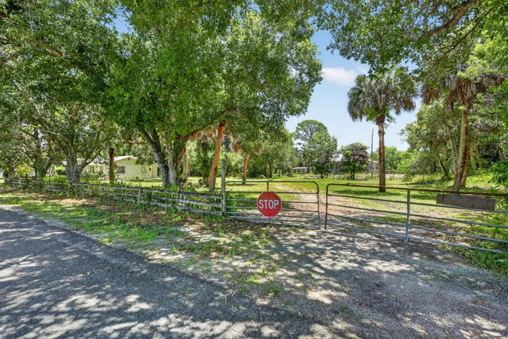 Expansive gated property featuring mature trees and a residential structure in the background