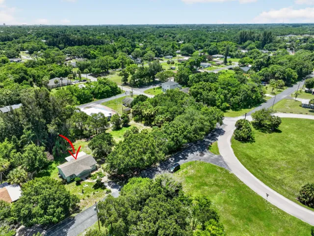 Aerial perspective showcasing a single-story residence with a light-colored gabled roof and surrounding mature trees