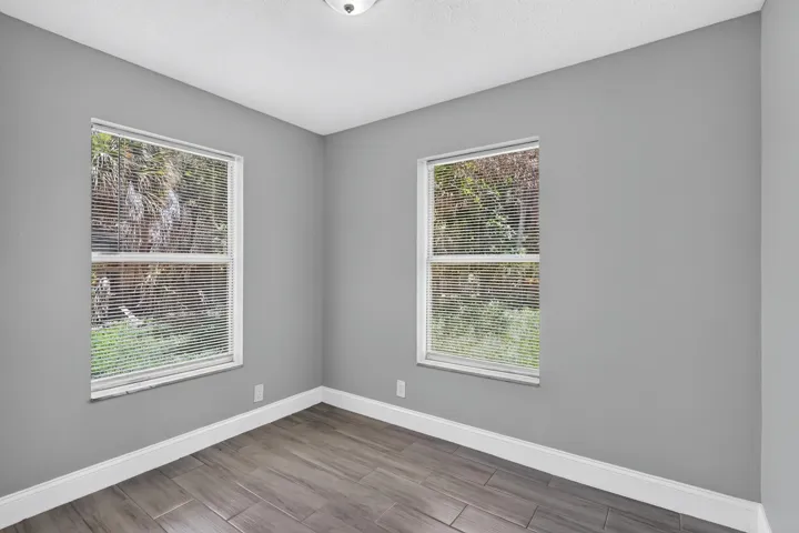 Bright interior room featuring two windows with horizontal blinds, grey wall paint, wood-finish flooring, and white baseboards