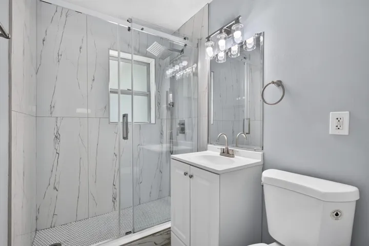 Contemporary bathroom featuring a spacious glass-enclosed shower with large format tile surround and white penny tile flooring