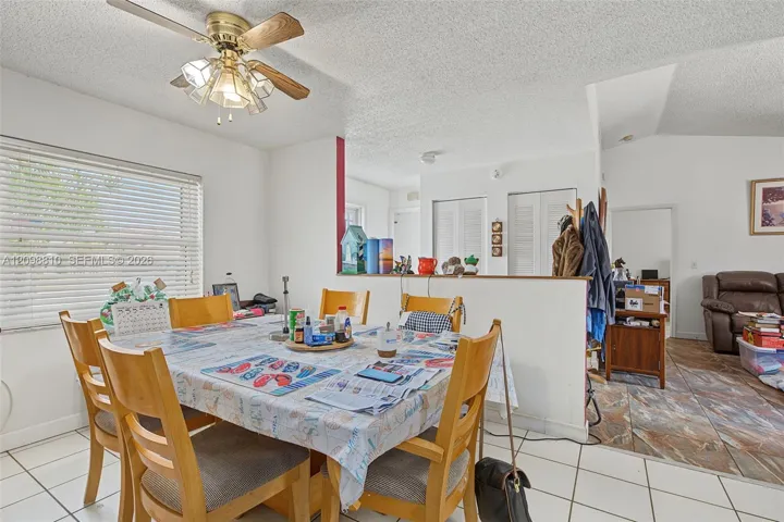 Dining area featuring a vaulted ceiling, white ceramic tile flooring, and a multi-light ceiling fan with integrated wood-finish blades
