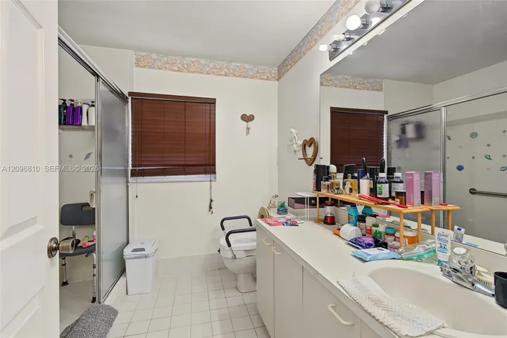Full-width vanity with an integrated sink, expansive wall-mounted mirror, walk-in shower with a sliding glass door, and tile flooring