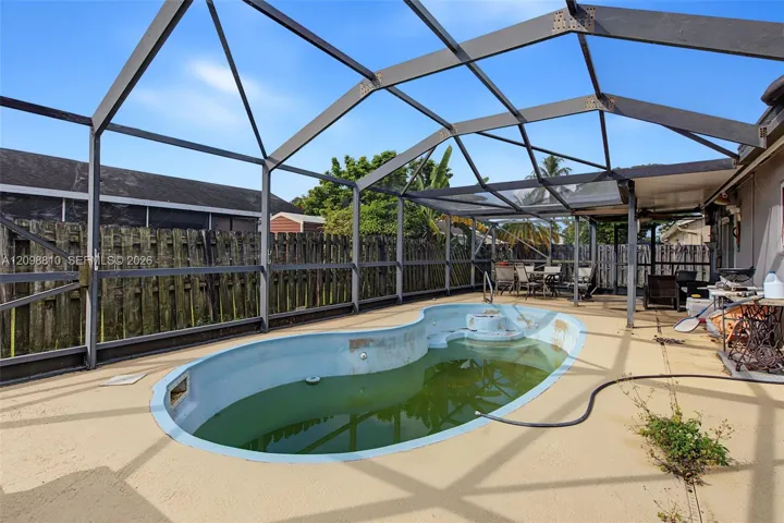 In-ground swimming pool enclosed by a screen lanai with a concrete pool deck and wood perimeter fencing