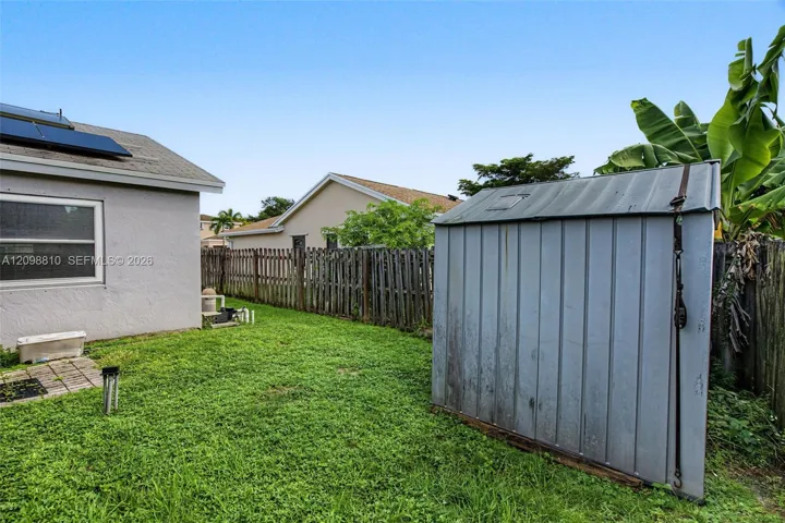 Rear exterior space featuring a fenced lawn, metal storage structure, and roof-mounted solar panels