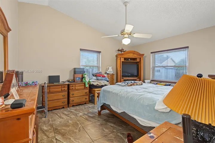 Vaulted ceiling, stone-finish tile flooring, ceiling fan with integrated lighting, and dual windows with horizontal blinds