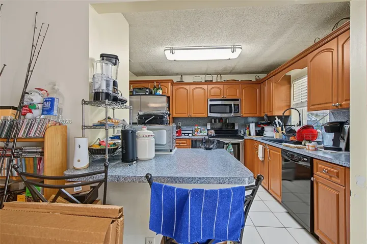 Kitchen featuring wood cabinetry, solid-surface countertops, built-in microwave, under-mount sink, and ceramic tile flooring