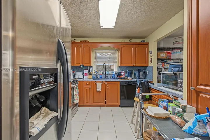 Kitchen featuring wood cabinetry, stainless steel refrigerator, matte black kitchen faucet, tile flooring, and a recessed pantry