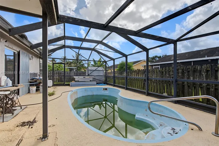 Screened-in patio featuring an in-ground swimming pool with integrated steps and a metal handrail, enclosed by a dark-frame pool cage and surrounded by a privacy fence