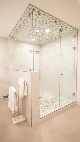 Glass-enclosed shower with tile flooring and ceiling, featuring large format wall tiles and recessed lighting
