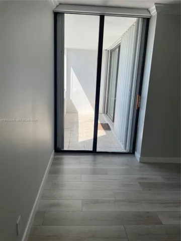 Sliding glass door with black frame, wood-finish flooring, and private balcony with tiled flooring
