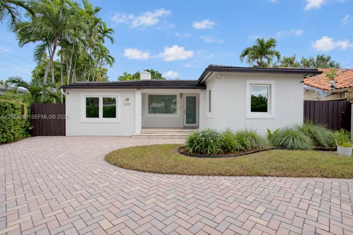 Single-story residence featuring a smooth stucco exterior, herringbone-pattern paver driveway, covered front entryway, and mature landscaping