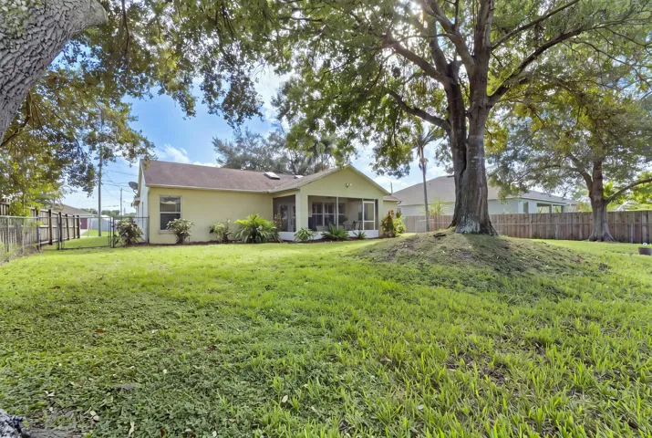 Expansive backyard featuring a large mature tree, manicured lawn, perimeter wood fencing, and a covered screened-in patio