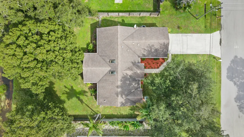 Aerial perspective of residential property featuring an asphalt shingle roof, two skylights, concrete driveway, and expansive lot with mature trees
