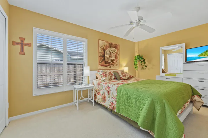 Bedroom featuring white plantation shutters, neutral carpeting, and a white ceiling fan with integrated lighting