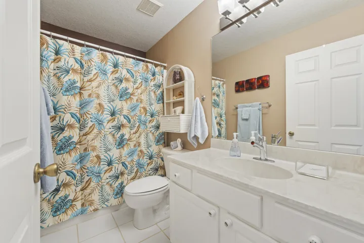 Bathroom featuring a white vanity cabinet with a light-toned countertop, integrated oval sink, full-width wall mirror, and overhead multi-light fixture