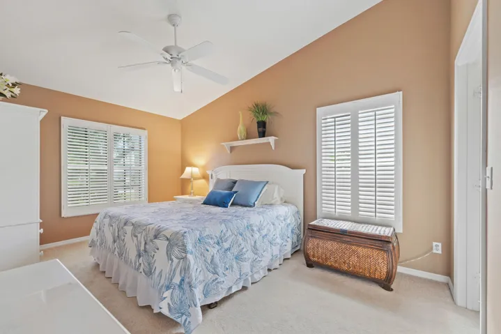 Vaulted ceiling featuring a ceiling fan, dual windows with plantation shutters, and a wall-mounted floating display shelf